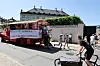 Demonstrationslastbil med banner kører gennem gaden omgivet af fodgængere og cyklister.