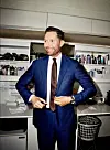 Kåre Quist i blåt jakkesæt i sminkerum med produkter på hylderne bag ham.