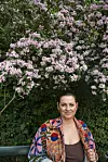 Karen-Helene Hjort på bænk foran stor busk med lyserøde blomster i park