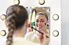 Sælma lægger makeup foran et lyst sminkespejl med rundtlys