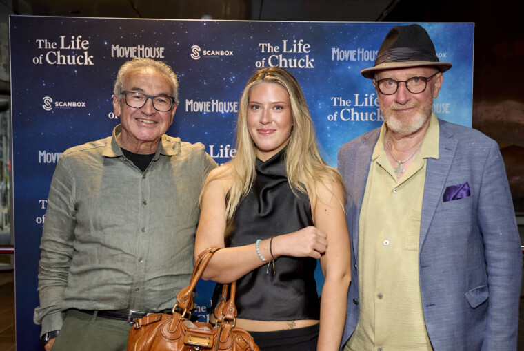 Tre gæster står foran blå fotovæg ved premiere på filmen 'The Life of Chuck' i MovieHouse.