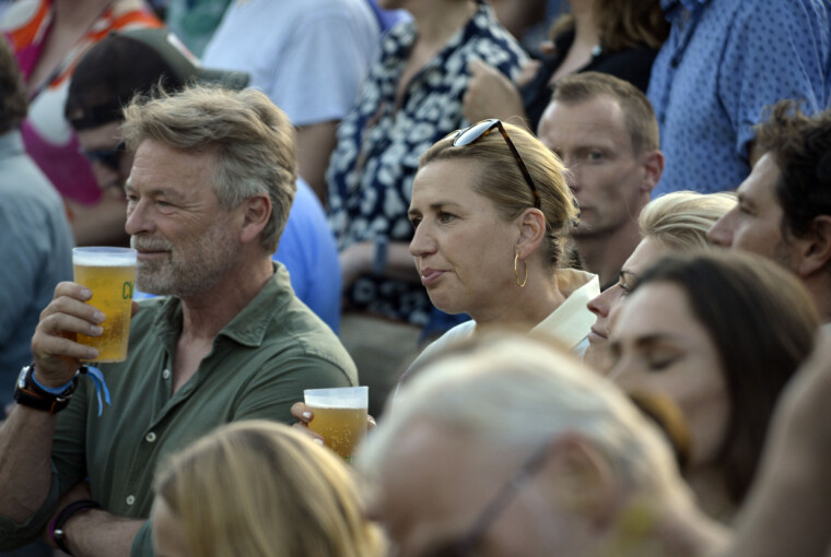 Publikum står tæt og drikker øl til en udendørs koncert.