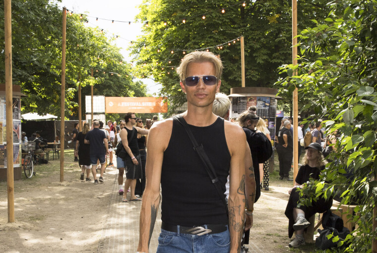Person står med øl på festivalsti omgivet af træer og andre gæster på Roskilde Festival.