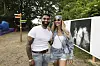 Smilende par poserer sammen på udendørs festivalområde med kunstplakater i baggrunden.