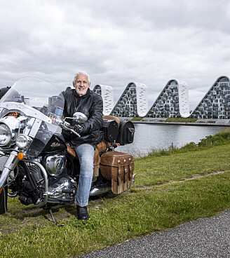 Verner Buhl sidder på en stor motorcykel ved vandet med karakteristiske bølgebygninger bagved.