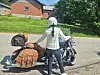 Person med hvid hjelm står ved stor motorcykel med lædertasker på solrig landevej