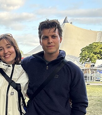 Tre personer står sammen på en festivalplads omgivet af telte og græs