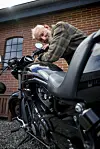Lasse Korsgaard står ved en sort motorcykel foran en rød murstensvæg.