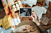 Gravid kvinde holder ultralydsbillede over sin mave omgivet af babyudstyr på gulvet