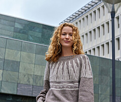 Kvinde i striktrøje står udendørs foran moderne bygninger