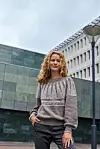 Kvinde i striktrøje står udendørs foran moderne bygninger