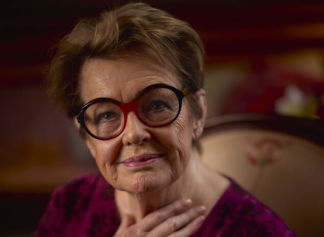 Skuespillerinden Ghita Nørby sidder indendørs med hånden mod brystet og ser mod kameraet.