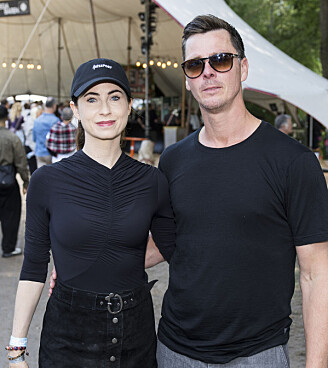 Par står arm i arm foran telt og langborde på udendørs festivalområde.