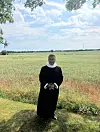 Præst i sort kåbe står foran kornmark på solrig dag