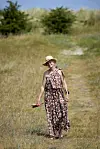 Annette Heick går barfodet på en sti i klitlandskab med stråhat og lang blomsterkjole.