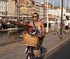 Kvinde på cykel med blomsterkurv kører langs Nyhavns kanal i aftensol