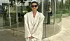 Sara Lauridsen i lyst, oversized jakkesæt med solbriller foran buet glasfacade