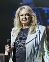 Bonnie Tyler står på scenen med mikrofon og hvid jakke under koncert i Berlin.