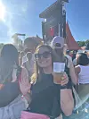 Smilende festivalgæst holder plastkrus med øl foran stor Tuborg-scene i solskin.