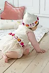 Baby kravler på lyst trægulv iført hæklet vest og hue med blomster