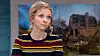 Kvinde i tv-studie foran billede af ødelagt bygning på skærmen bag hende.