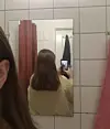 Person tager spejl-selfie på badeværelse med skulderlangt hår set bagfra.