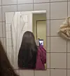Billede af person med langt, mørkt hår fotograferet i spejl i badeværelse.