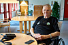 Allan Petersen i kørestol ved rundt bord på lyst plejecenter med telefon foran sig