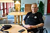 Allan Petersen i kørestol ved rundt bord på lyst plejecenter med telefon foran sig