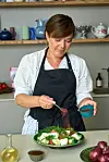 Louisa Lorang står i sit køkken og drysser krydderi over en grøn salat på en tallerken.