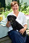 Louisa Lorang sidder i haven med en lille sort hund på skødet ved et udendørs bord.