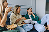 Tre unge kvinder sidder i sofaen og deler popcorn under en hyggelig filmaften.