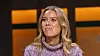 Kvinde i lilla striksweater sidder foran en orange oplyst baggrund.