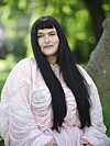 Emilie Foli med langt mørkt hår i lyserød kjole sidder ved et træ i en grøn park.