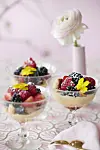 Dessertglas med trifli, sommerbær og gule blomster på lyserødt bord