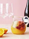 Glaskande med juice og jordbær foran to vinglas og en vinflaske.