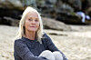 Ældre kvinde i stribet trøje sidder alene på en rolig sandstrand.