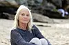 Ældre kvinde i stribet trøje sidder alene på en rolig sandstrand.