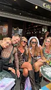 Gruppe i festtøj sidder tæt sammen ved borde foran en café og smiler mod kameraet
