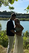 Par står og omfavner hinanden ved en sø omgivet af grønne træer