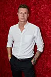 Mand i hvid skjorte står foran rød væg af blomster ved 'Bachelorette' 2026-finale.
