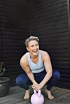 Smilende kvinde i træningstøj sidder på terrasse og holder en lyserød kettlebell.