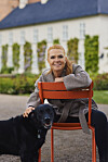 Inger Støjberg på rød stol klapper sort hund foran lys bygning med grønne planter