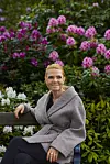 Inger Støjberg på bænk i park foran lyserøde og hvide rhododendron