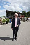 Henrik R. Petersen i jakkesæt på vej foran tribunebygning med mennesker bagved