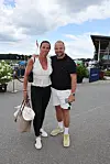 Par står på vej foran sportsanlæg med telte og flag på en skyet sommerdag