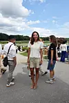 Kvinde i lyse sommerklæder står blandt gæster ved et udendørs arrangement på en solrig dag.