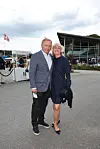 Smilende par står tæt sammen foran glasbygning ved udendørs arrangement.