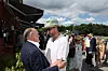 To mænd taler sammen foran en udendørs restaurant med gæster i baggrunden