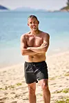 Mand i shorts står på sandstrand foran roligt turkisblåt hav